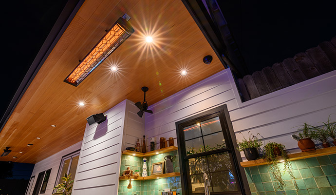 Ceiling-mounted radiant outdoor patio heater installed on a wooden soffit with recessed lights.