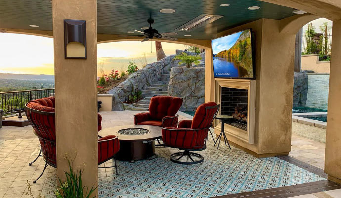 Covered outdoor cabana patio with ceiling speakers, TV over fireplace, and fire pit lounge.