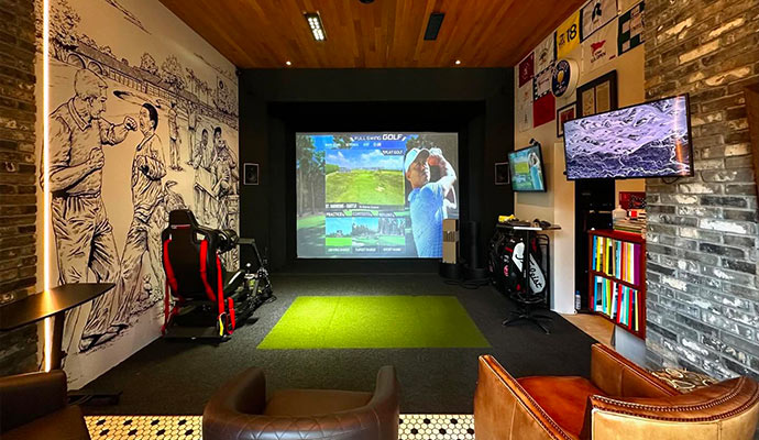 Full Swing golf simulator entertainment lounge with turf mat and leather armchairs.