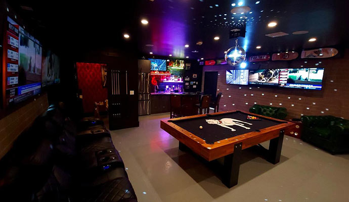 Entertainment game room lounge featuring a custom pool table, bar, and multiple TV screens.