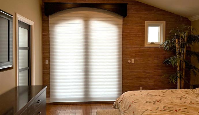 Cozy bedroom with textured brown wallpaper, a dark wood valance, and a large white fabric window shade