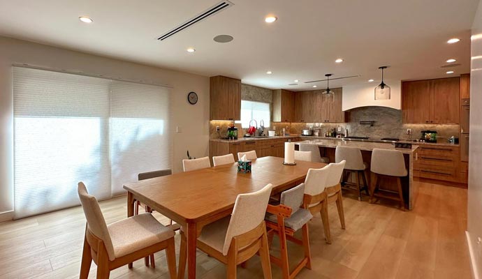 Modern open-concept dining room with a large light wood table and eight chairs, leading into a kitchen with matching wood cabinets