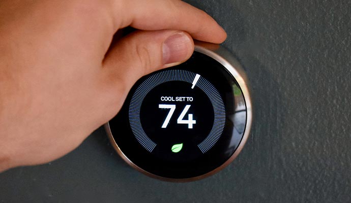 Person adjusting a smart thermostat Person adjusting a smart thermostat mounted on a wall