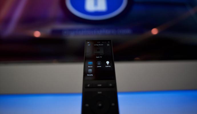 Smart remote control for lighting and security Close-up of a smart remote control with options for lighting and security in front of a large screen display.