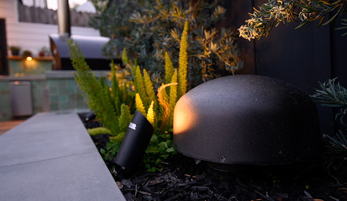 In-ground landscape subwoofer and directional landscape light nestled in garden greenery.