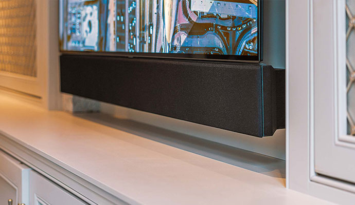 Low-angle view of a sleek black soundbar custom-mounted flush beneath a flat-screen television