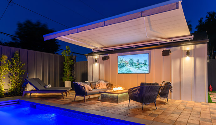 Motorized retractable outdoor patio awning extended over a poolside lounge with fire pit table.