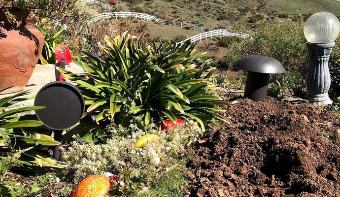 Landscape audio system with satellite speaker and dome subwoofer installed in a garden hillside.