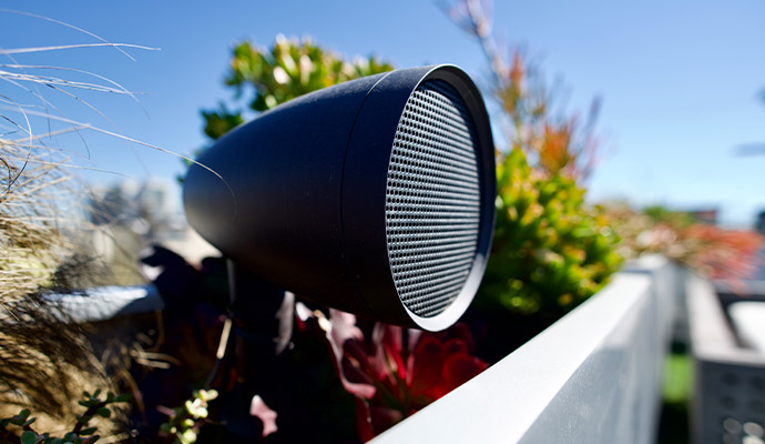 Close-up of a bullet-style outdoor landscape audio speaker mounted in a planter box.