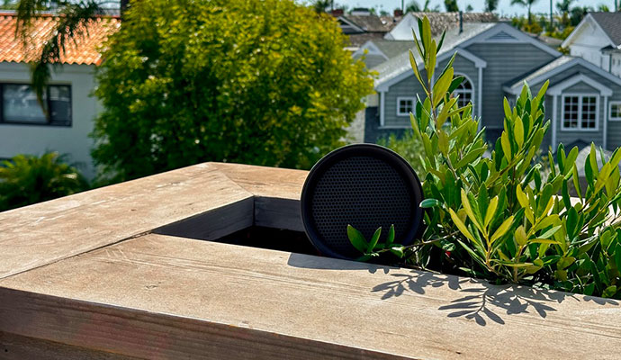 Black outdoor speaker installed in a wooden planter.