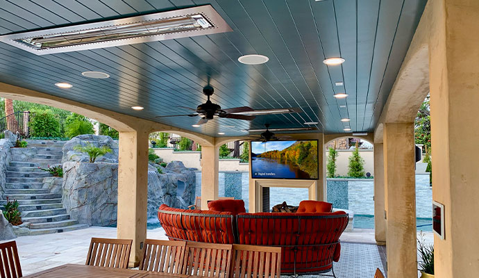 Covered outdoor patio with wall-mounted TV, ceiling speakers, and a control panel.