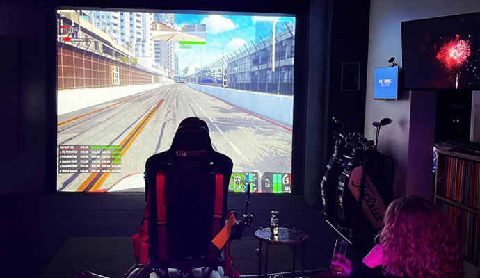 Interactive racing simulator setup with racing bucket seat and panoramic screen display.