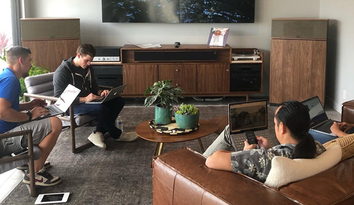 Team using laptops in a living room with home audio equipment.