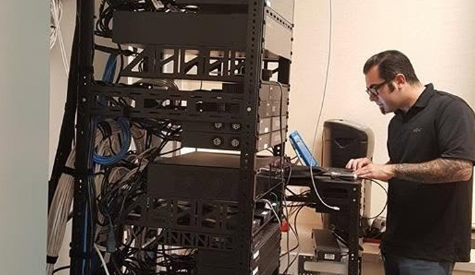 Technician using a laptop beside a network equipment rack.